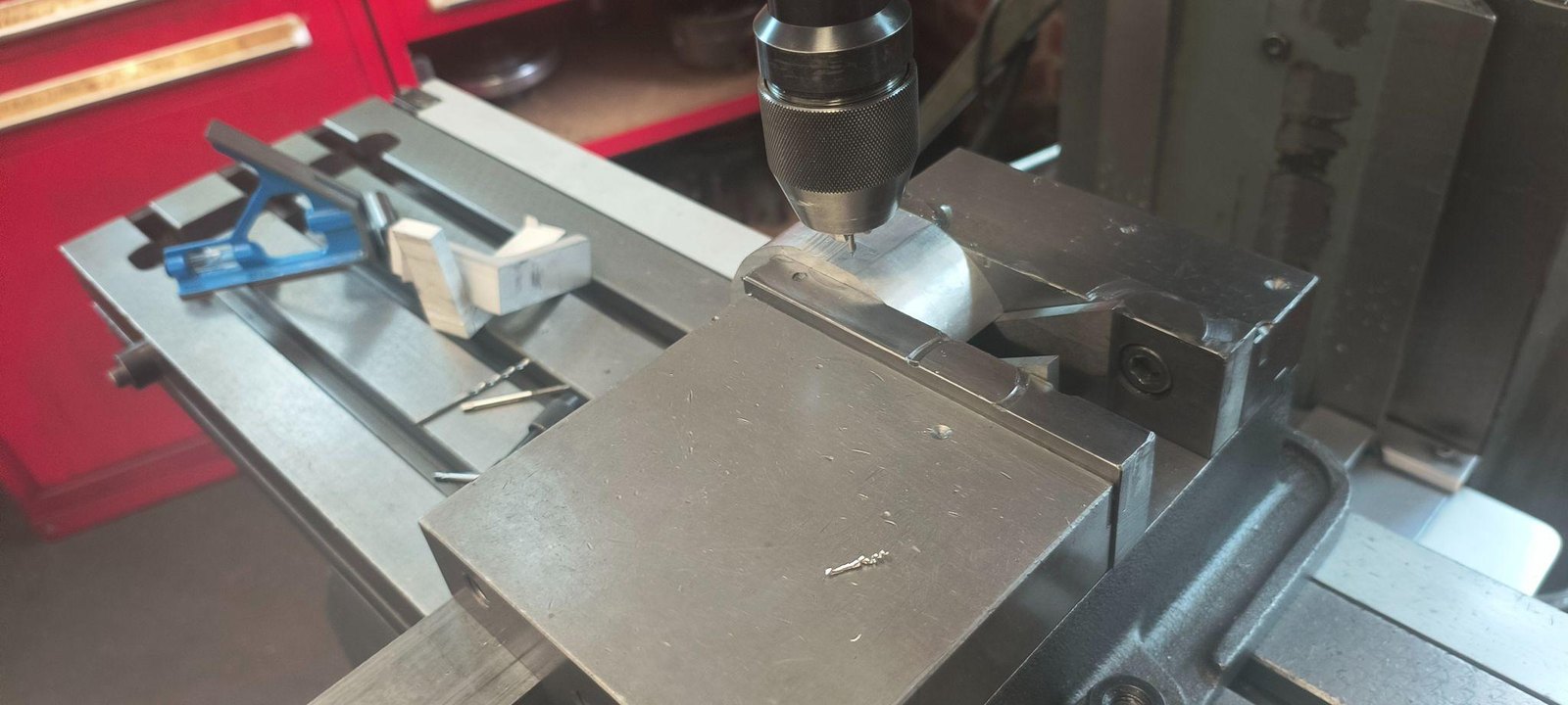 A part held against angle blocks on the drill press table.
