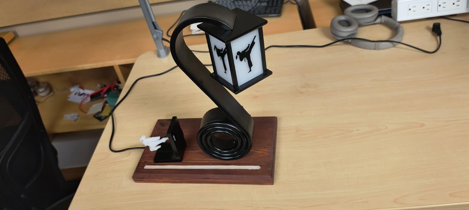 The finished lamp lit on a desk, the lantern glowing and the coil holding the books.