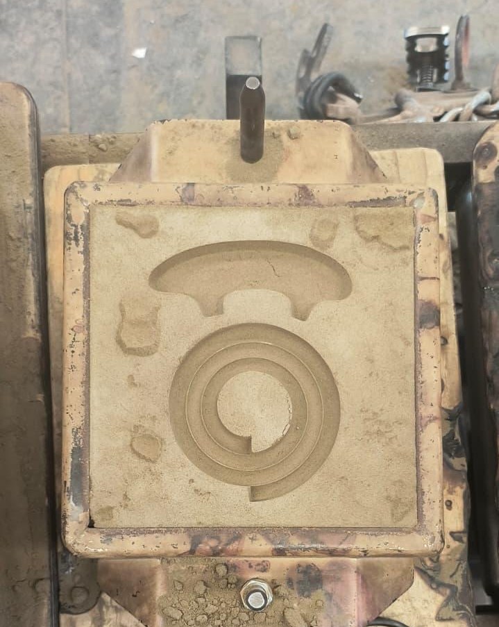 The closed sand mould in its flask, the coil impression visible in the parting face.