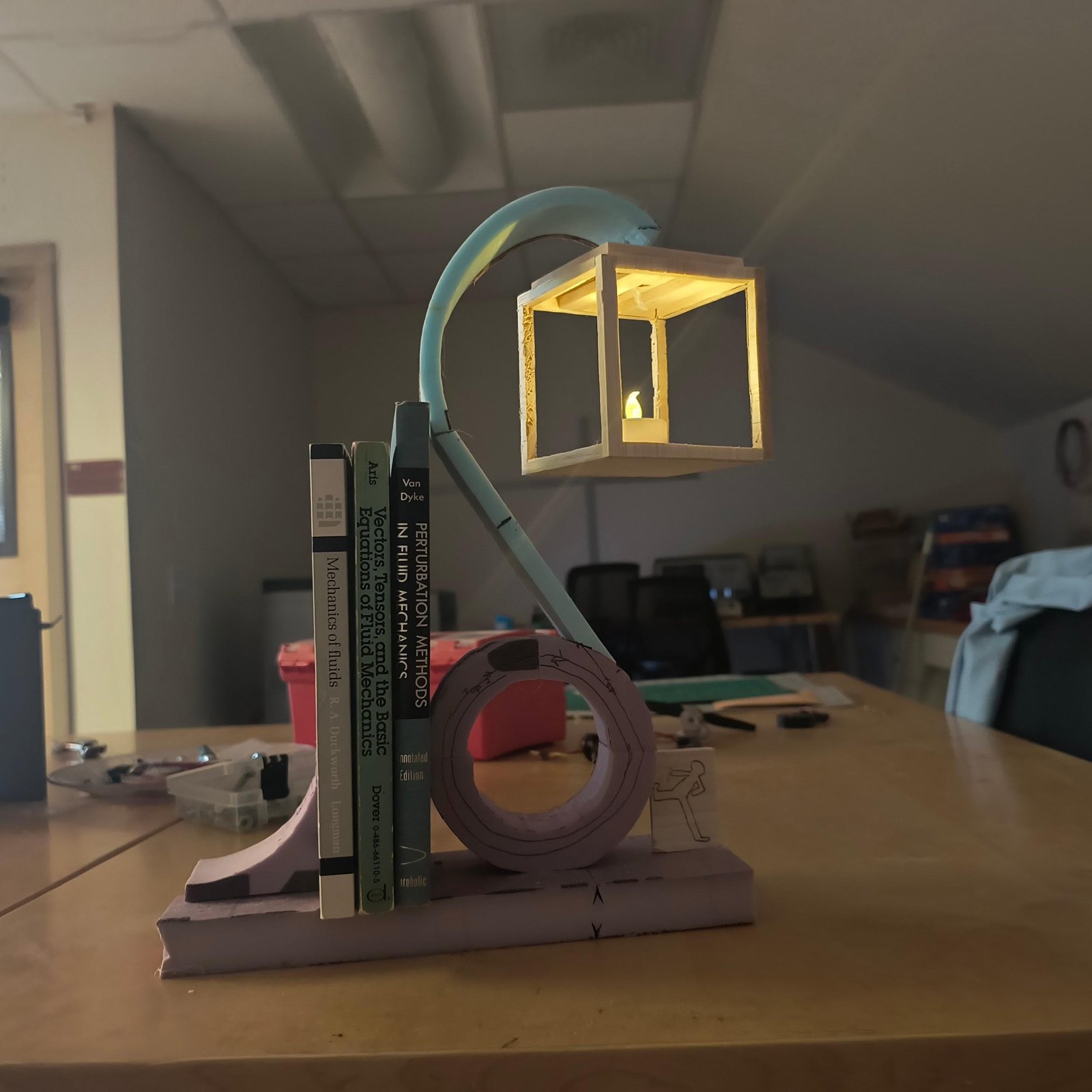 A mock-up in foam and board, lit from inside, standing beside books on a bench.