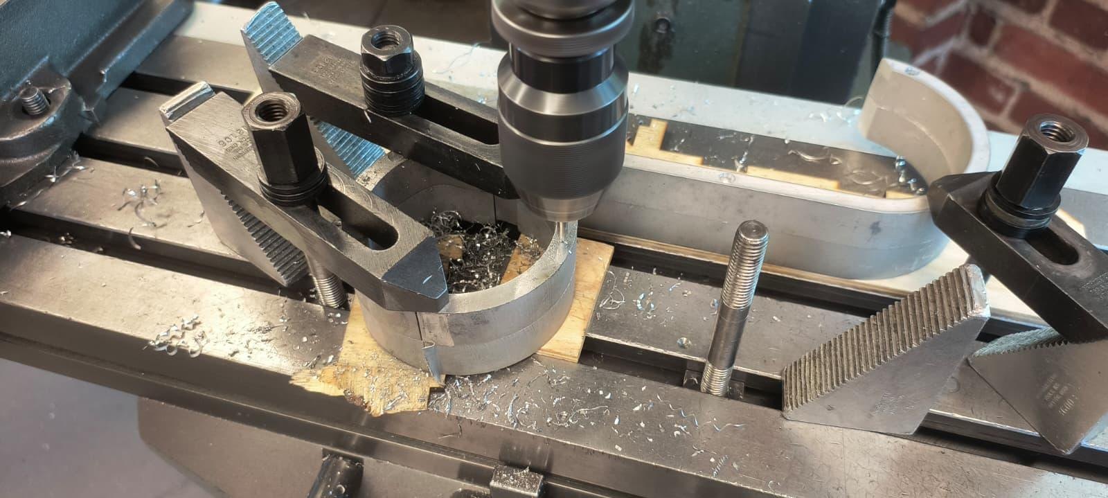 A coil backing clamped to the mill table under strap clamps, being drilled.