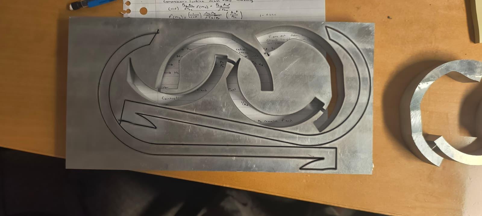 The arm and coil profiles cut through a sheet of aluminium plate on the waterjet, the parts still sitting in the sheet.