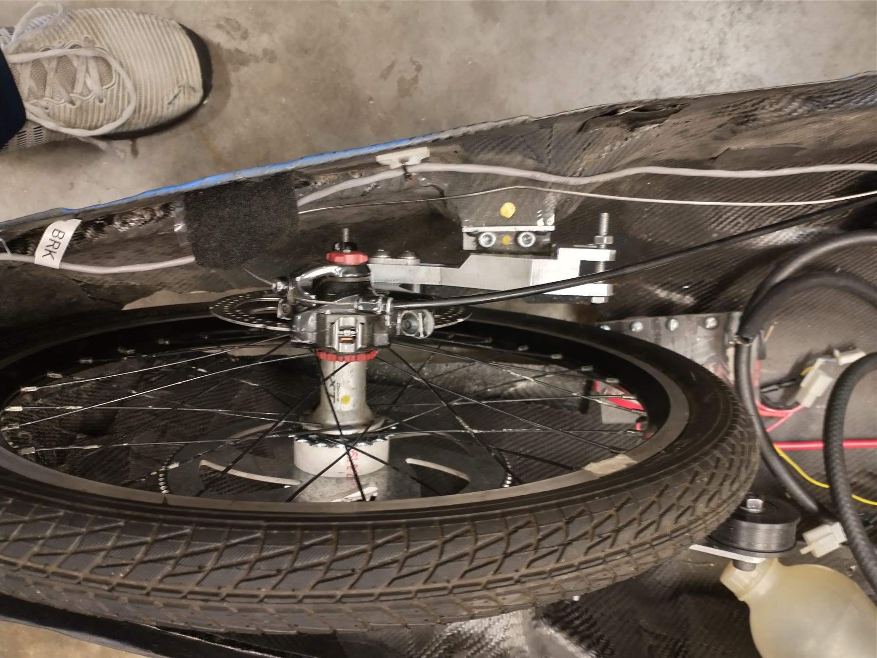 The rear wheel, brake and axle installed, photographed from below the carbon monocoque, with the adjuster bracket above.